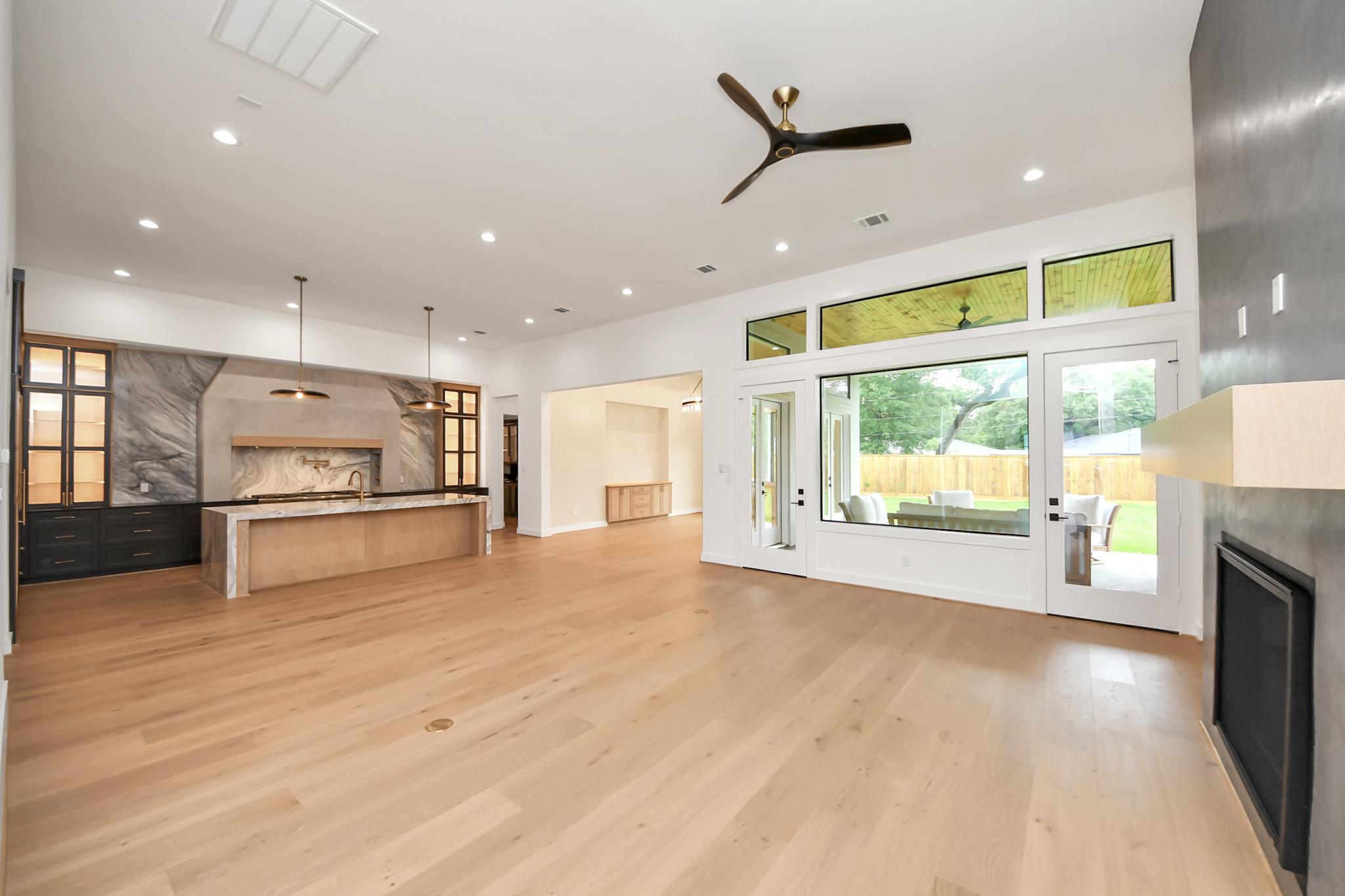 Open-concept warm contemporary kitchen and living room featuring Elite Tiles quartz waterfall island, white oak engineered flooring, and a modern fireplace.