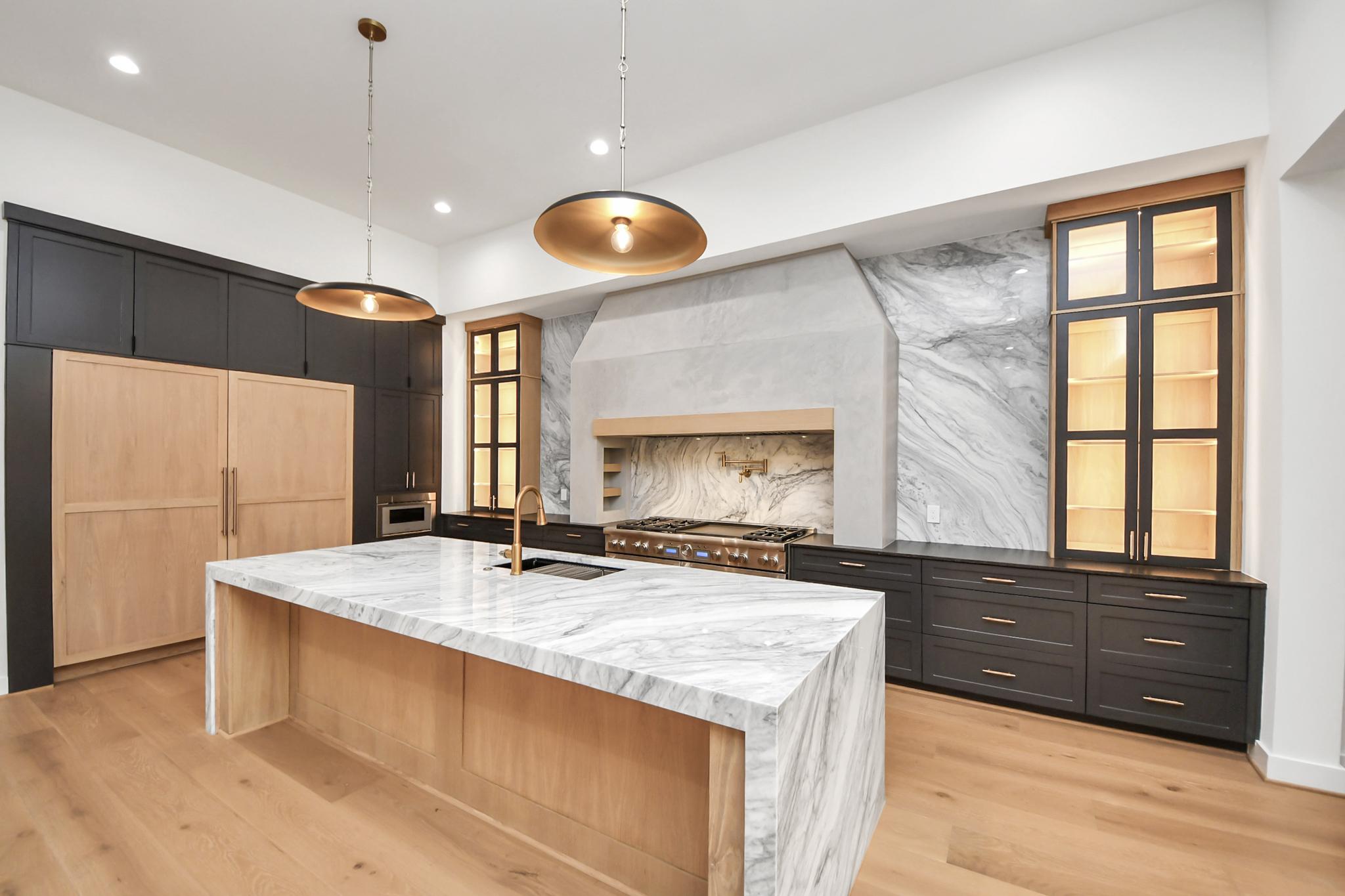 Luxurious warm contemporary kitchen featuring a large dramatic white marble quartz waterfall island, a grey textured plaster hood, and contrasting dark and light wood cabinetry.